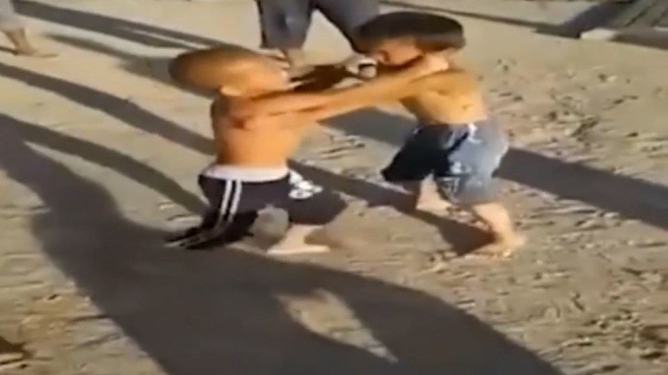 Gang of cruel adults look on and even pick the boys up when they fall to make them continue fighting