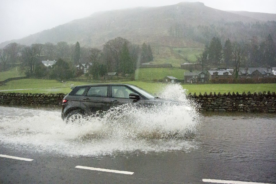 Car driving through floodwater on road during heavy rainfall, A591, Grasmere, Lake District, Cumbria, England, December