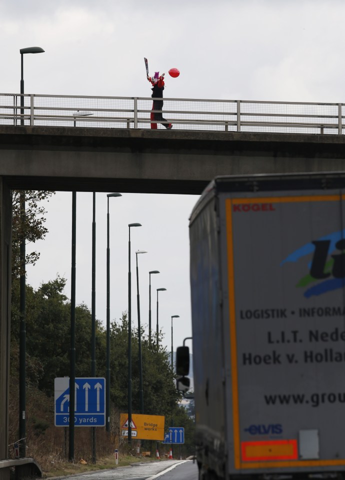FAMEFLYNET - Exclusive: The Killer Clown Craze Shows No Sign Of Slowing Down As An Individual Dressed As A Clown Brandishing A Sword Is Seen On A Bridge Taunting Traffic Below On The M20
