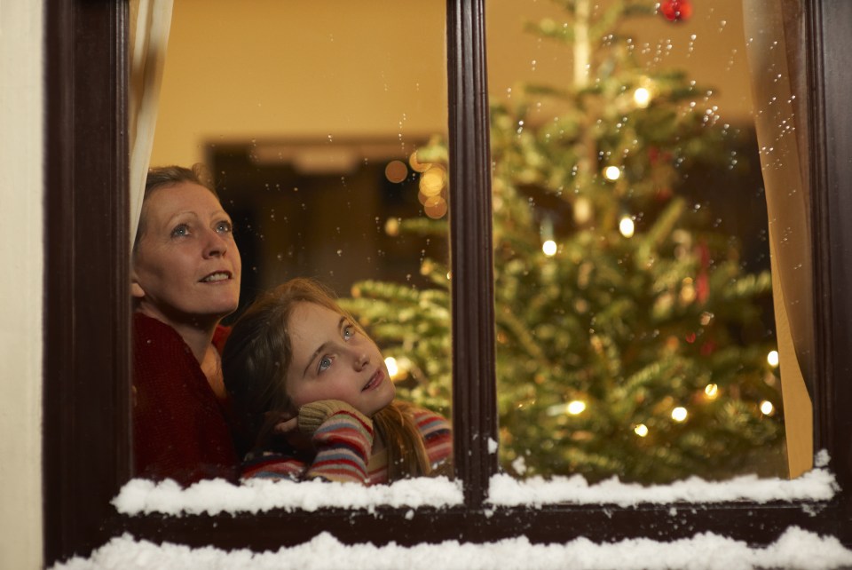 Girl and mother gazing out of window at christmas.
