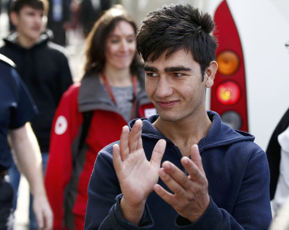 A young migrant claps as he is escorted off a coach by UK Border Force today