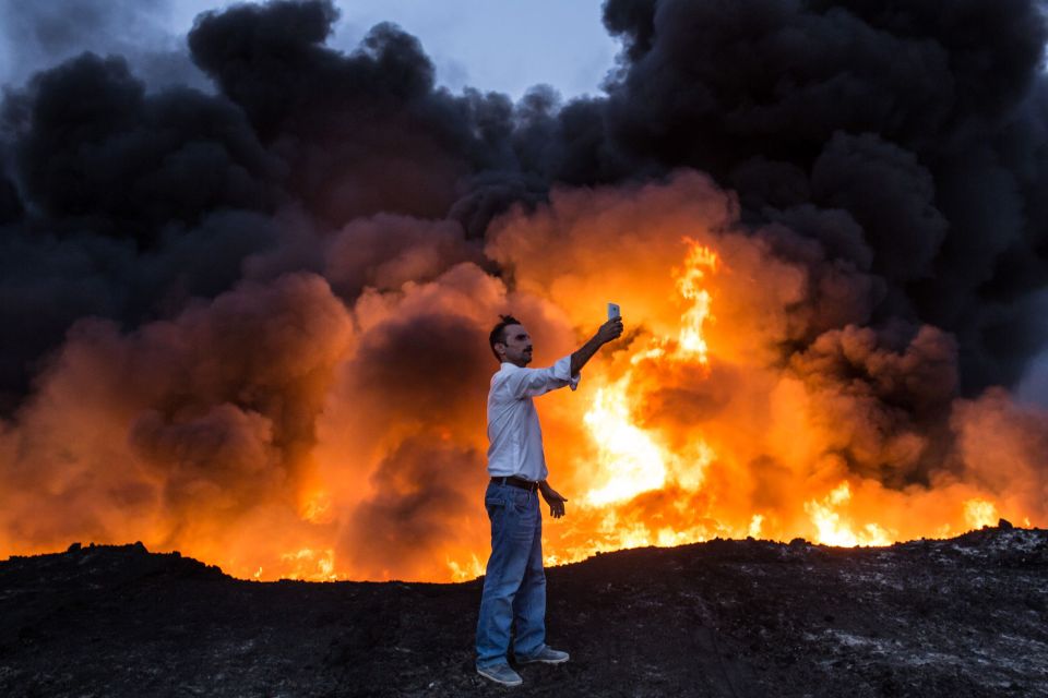 A man takes a selfie in front of a fire