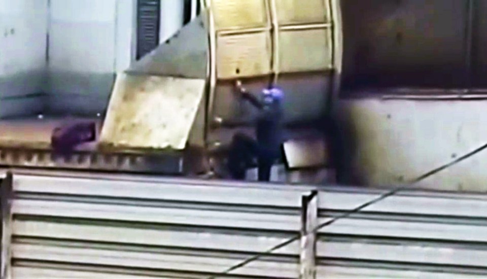 The man starts climbing the barrier so he could jump onto a train's roof