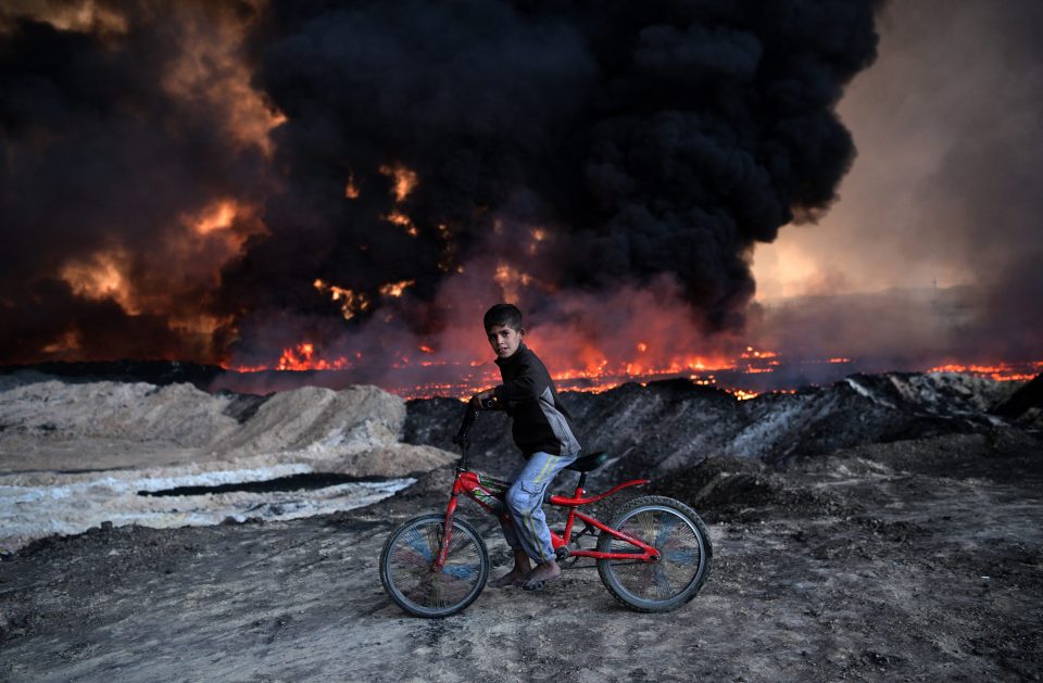 A boy pauses on his bike as he passes an oil field that was set on fire by retreating ISIS fighters ahead of the Mosul offensive