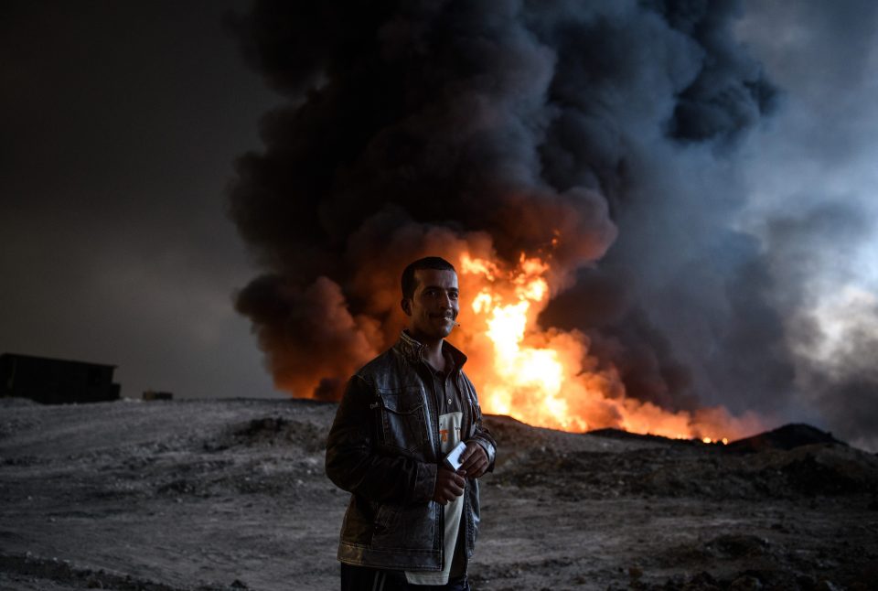A man smokes a cigarette stand next to an oil field that was set on fire by retreating ISIS fighters 