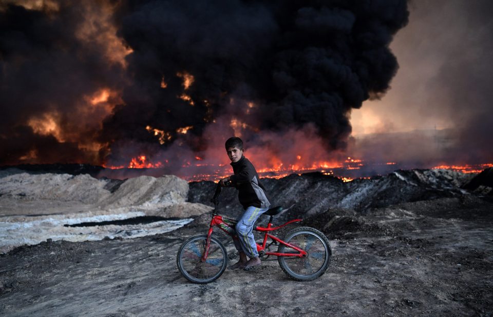 A boy pauses on his bike as he passes an oil field that was set on fire by retreating ISIS fighters 