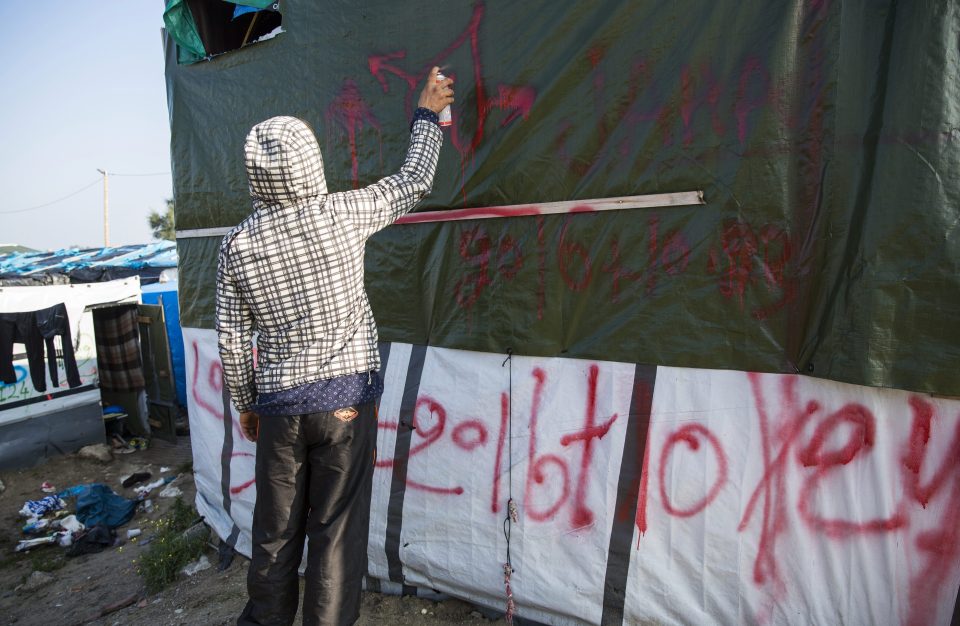 Migrants spraypaint a tent at the Jungle migrant camp with symbols and tomorrow's date - the date when authorities begin clearing the camp 