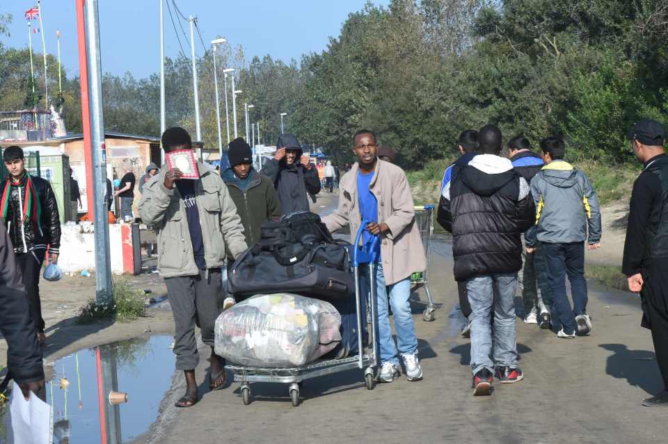 Migrants walk with their luggage through the temporary reception centre