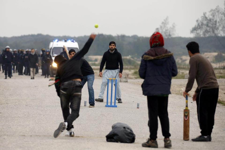 French CRS riot police secure a road as migrants play cricket on the eve of the evacuation