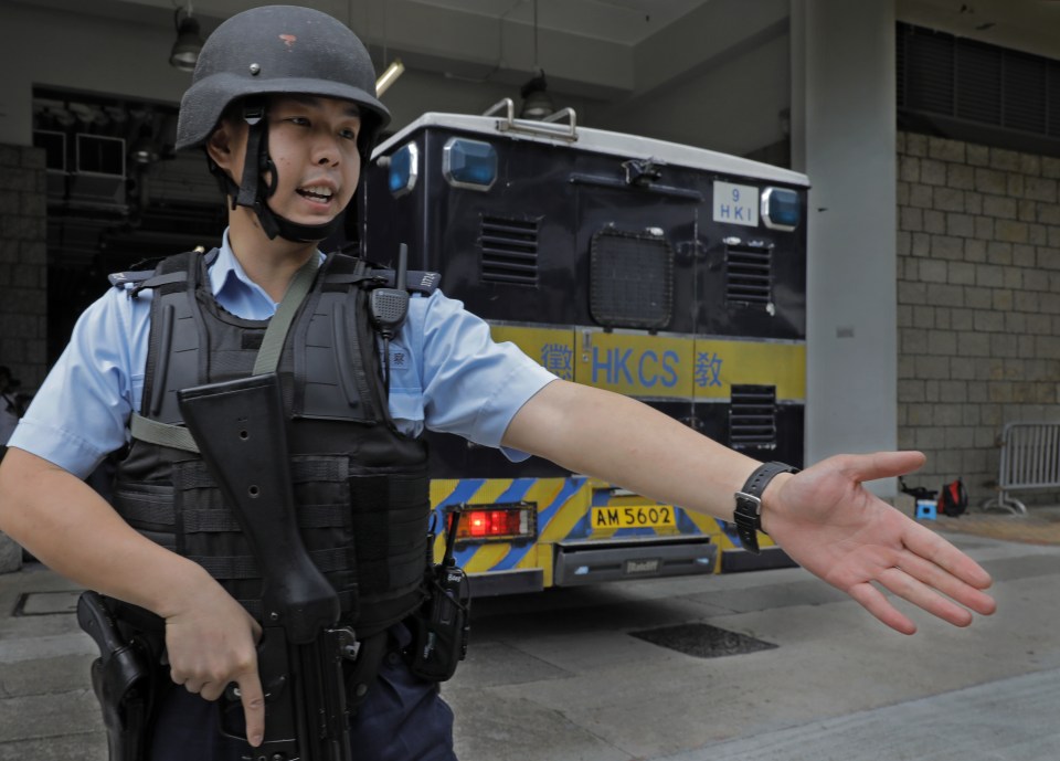 An armed officer gestures for the crowd to move back to make way for a bus carrying the former banker to court