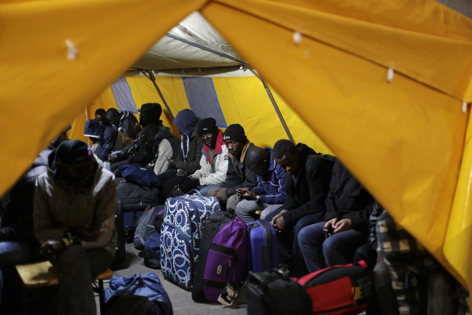 Migrants sit inside a tent as they are registered at a processing centre 