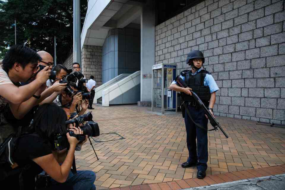 An armed policeman stands guard outside guard in front of members of the media