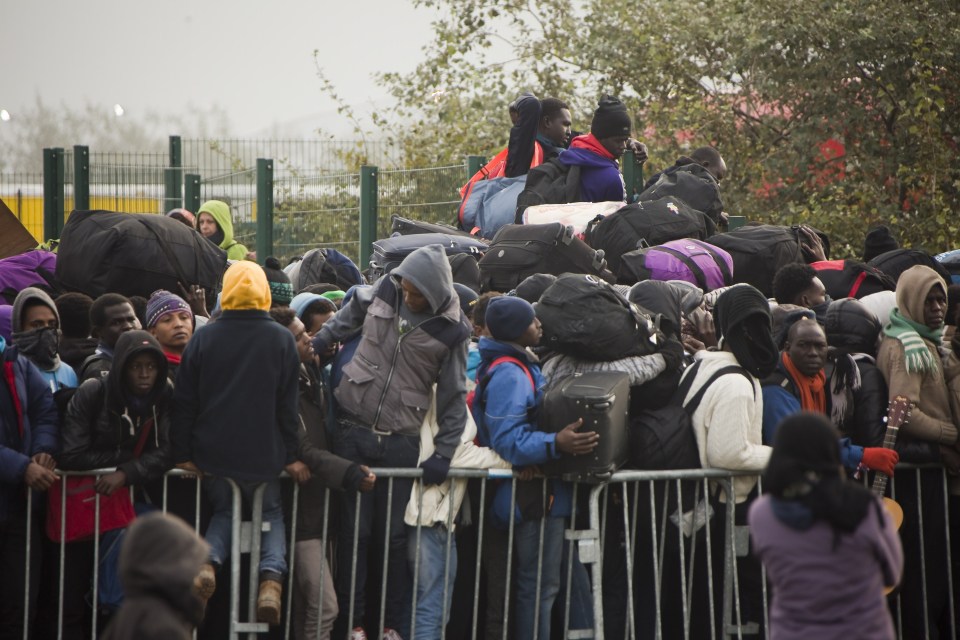 Refugees with their luggage wait to leave Calais 'Jungle' camp