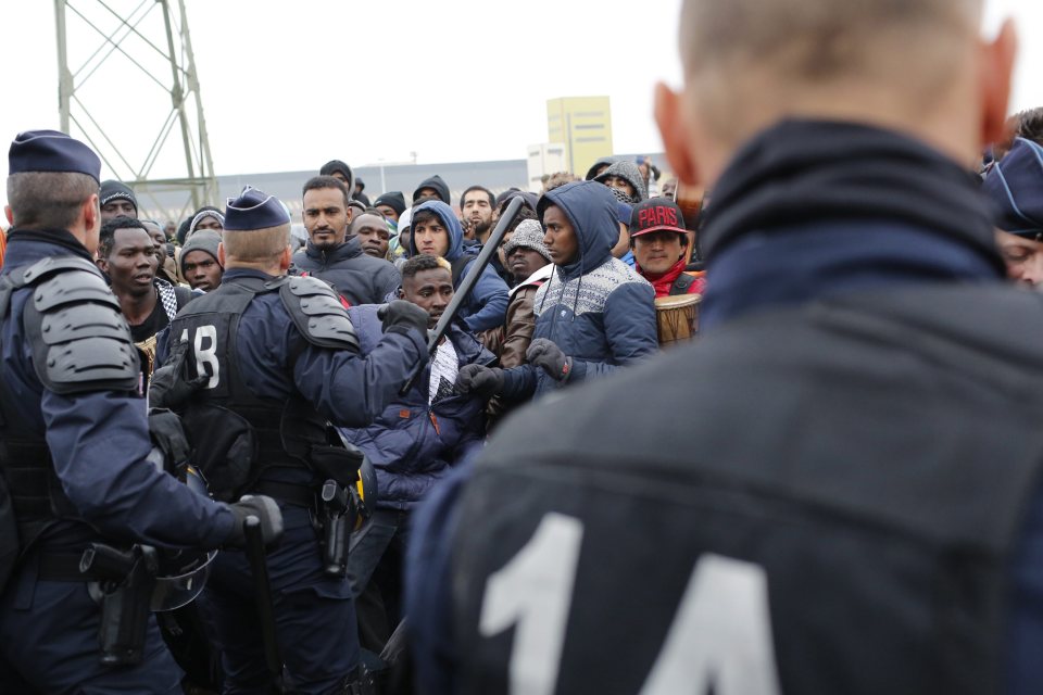 A police officer draws his baton amid scuffles with a crowd of migrants 
