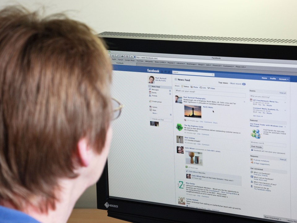 Modern everyday life scene of a mature woman using a computer for social networking looking at Facebook page on a website UK