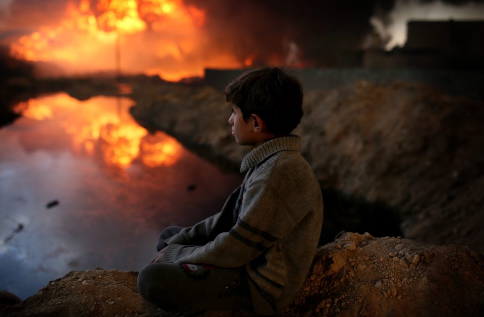  A boy looks on as fire fighters try to extinguish the fire at oil wells, were set on fire by ISIS as they fled Iraqi government forces