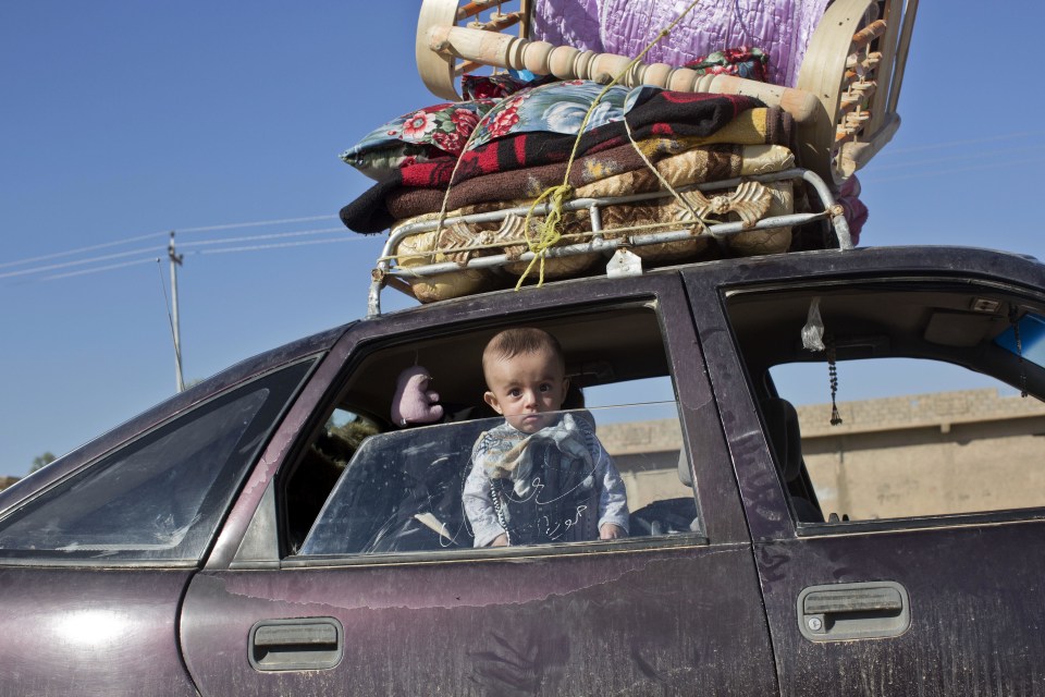 A baby peers out as his family flees Mosul with everything they can take strapped to the roof