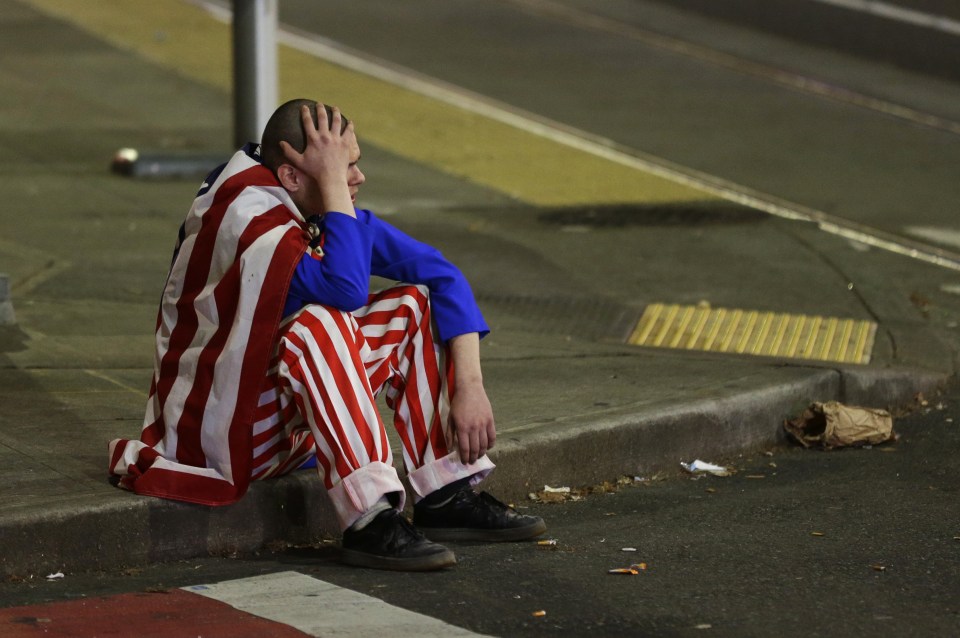 A man dressed in red-white-and-blue sits on the curb during a protest against President-elect Donald Trump