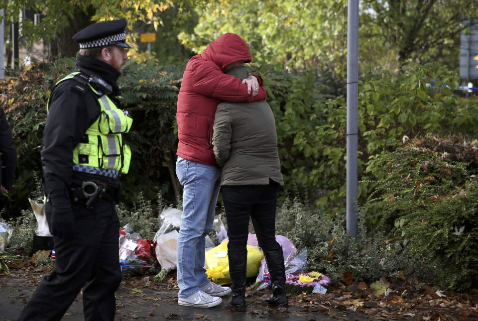 A police officer escorts mourners leaving floral tributes near the scene of an accident where a tram overturned killing 7 people and injuring 50 passengers in Croydon, south London