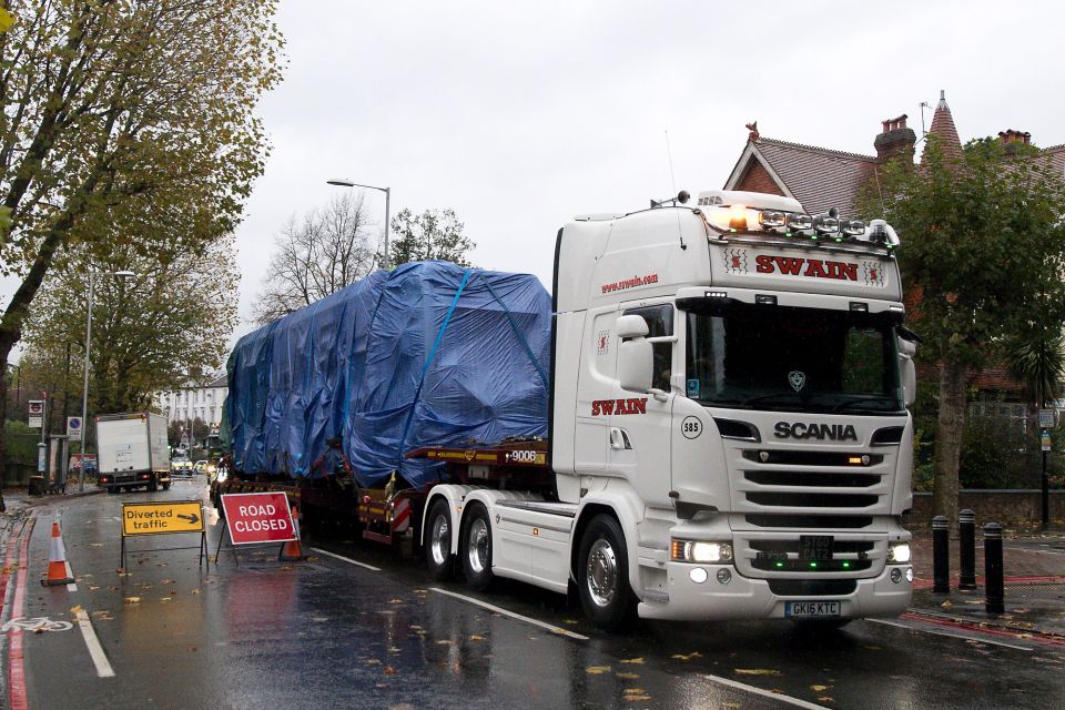 A tram carriage covered in tarpaulin is driven away from the scene of the accident on a truck in Croydon