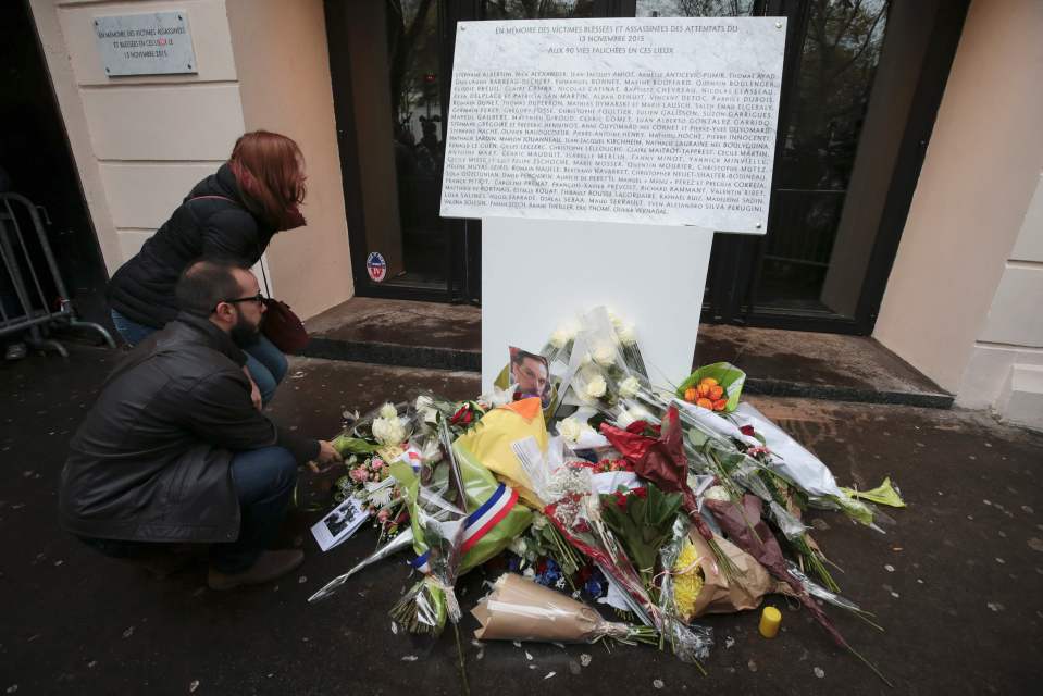 People lay under a commemorative plaque reading "In memory of the injured and killed victims of the attacks of November 13, 2015