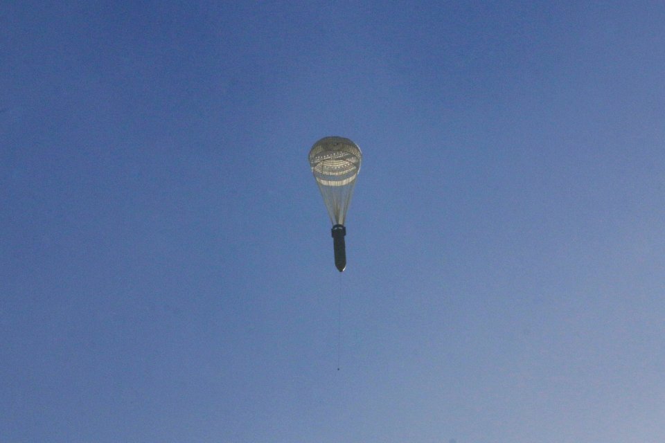 A parachute bomb falls out of the sky into a densely populated area