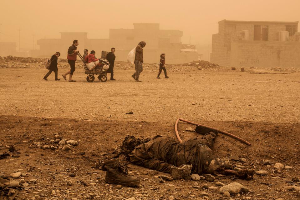  Locals pass close to the body of an Isis militant while fleeing from Mosul