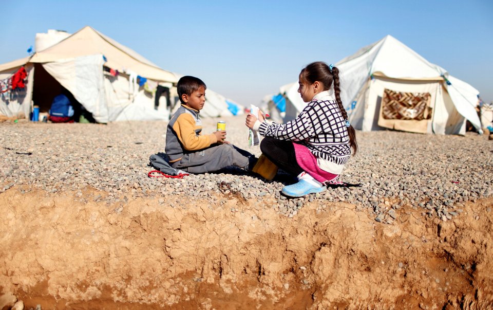 A displaced Iraqi girl who fled the Islamic State stronghold of Mosul, teaches her brother out side their tent at Hassan Sham camp, Iraq