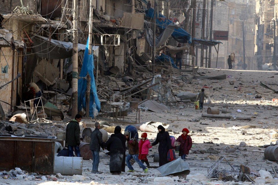 Syrians walk over rubble of damaged buildings, while carrying their belongings, as they flee clashes between government forces and rebels