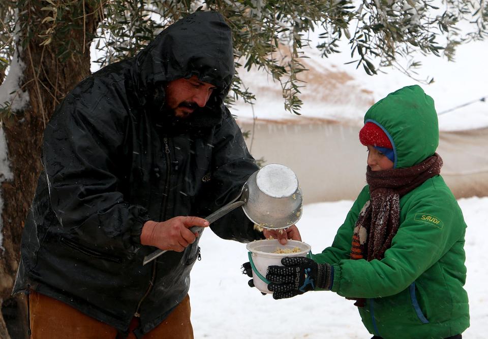 A Syrian boy receives food aid in a plastic bucket while in the tent city of Azaz