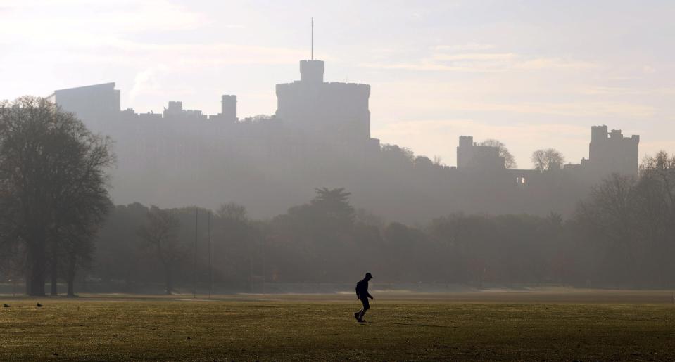  A runner jogs across the public sports fields of Home Park as fog surrounds the distinctive silhouette of Windsor Castle in Berkshire