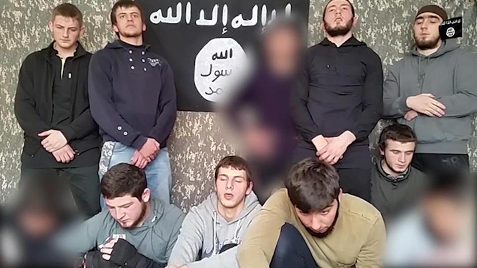 The Russians - some of whom appear to be just teens - in front of the black flag of ISIS