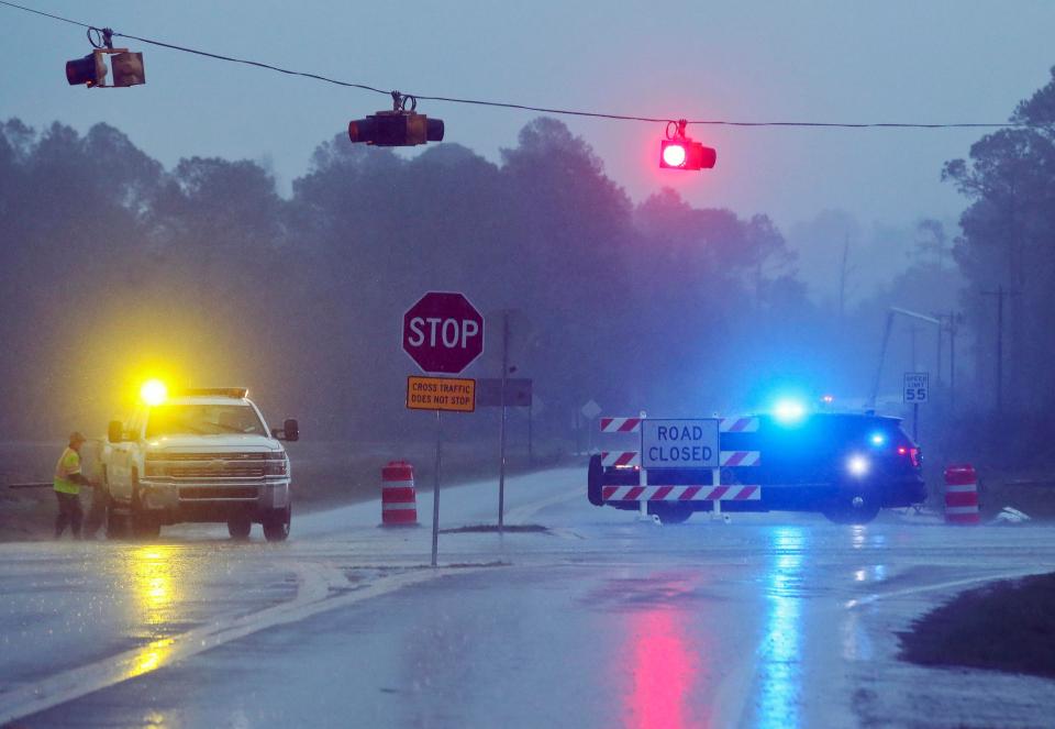 A Brooks County Sheriff and officials block Highway 122 as power line workers repair a downed pole in the background