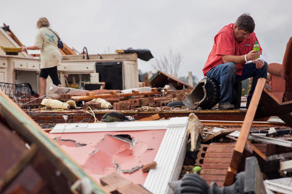 Jeff Bullard sits in what used to be the foyer of his home as his daughter, Jenny Bullard, looks through debris after the devastating tornado
