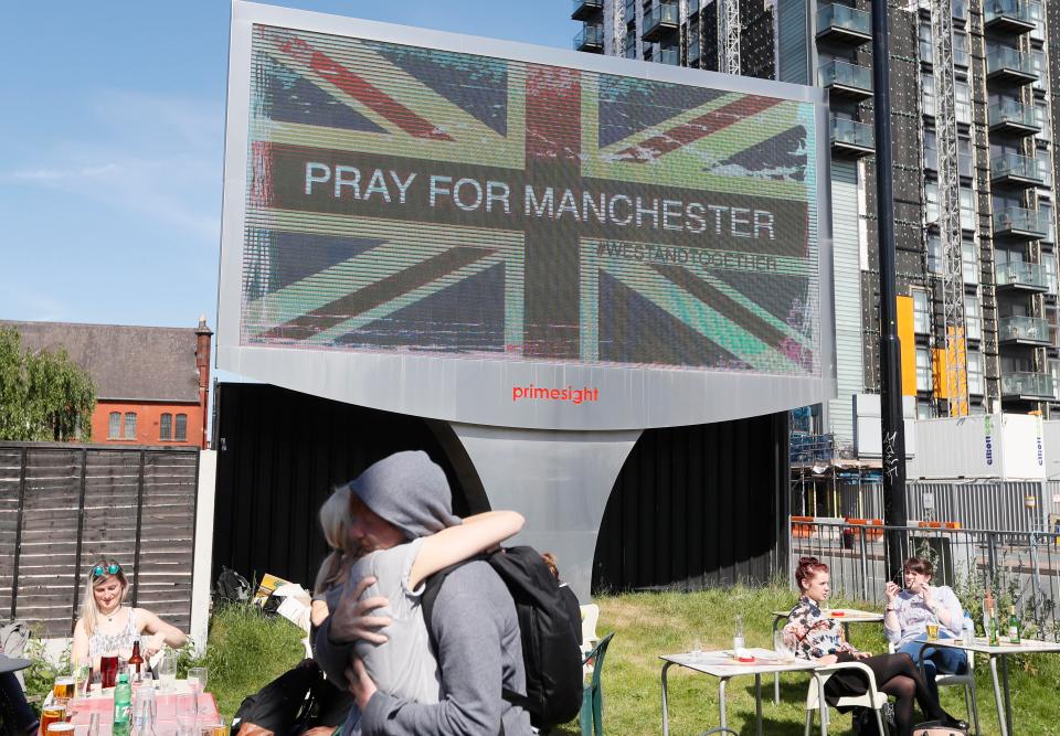 A couple embrace in front of a sign reading 'pray for Manchester'