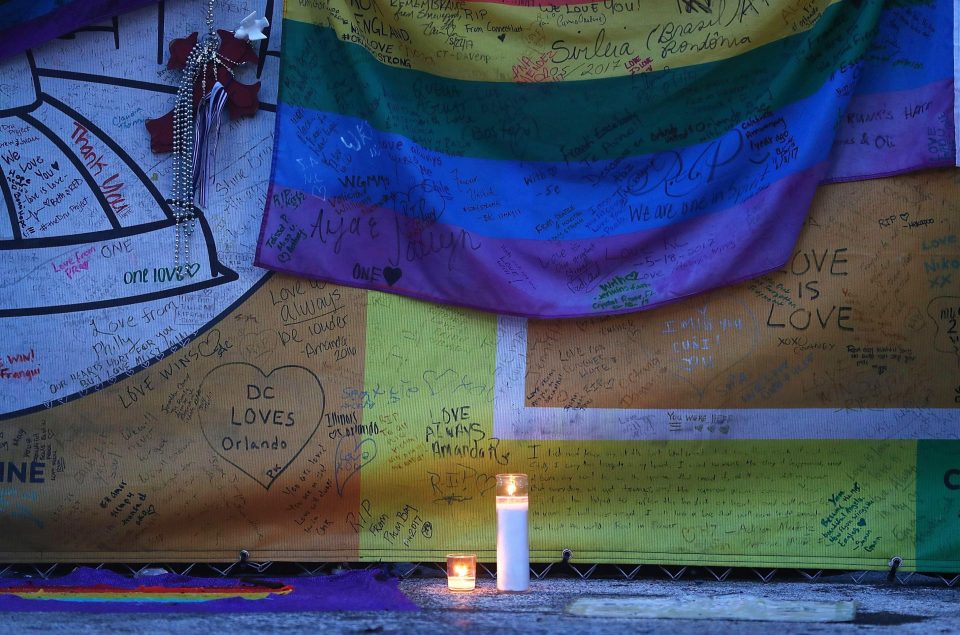 Candles burn in front of a rainbow flag