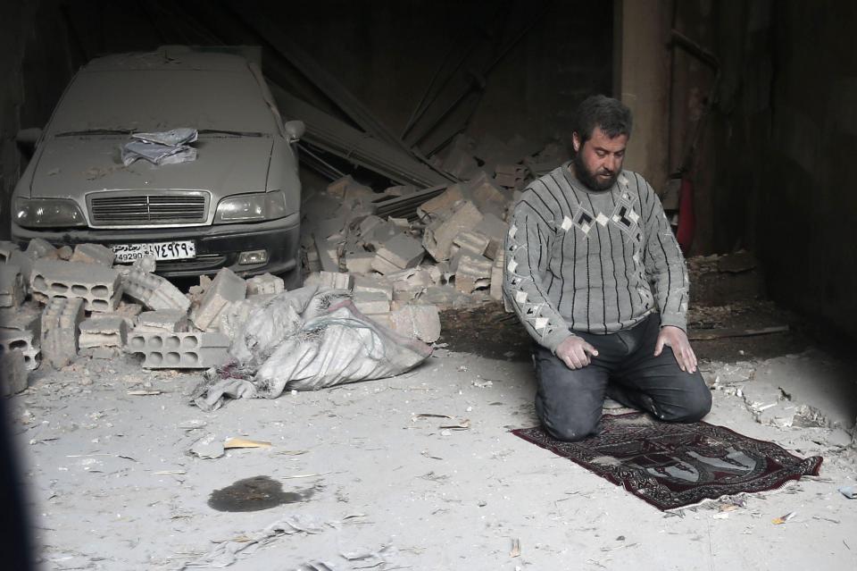 A Syrian man prays amid the rubble after an air strike