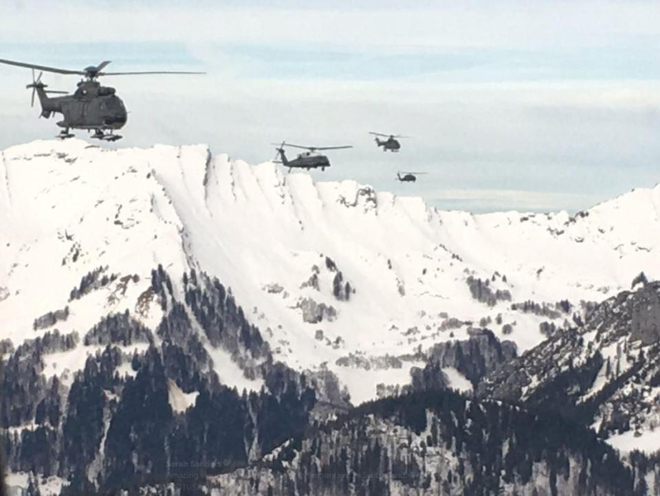 The formation of helicopters head toward the alpine village through stunning scenery 