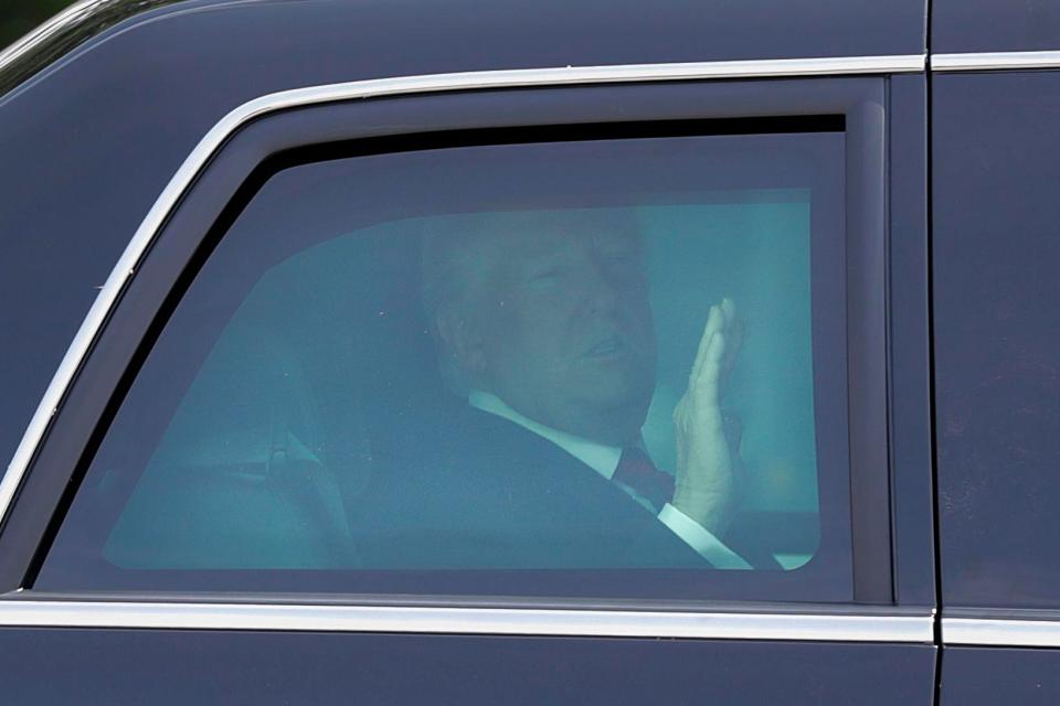 Donald Trump waves to photographers after leaving the air base in a limo after flying in from the G7 summit in Canada