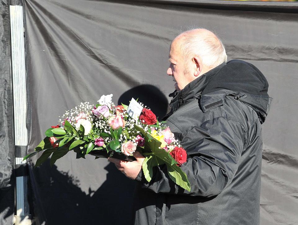 A floral arrangement is brought towards the grave