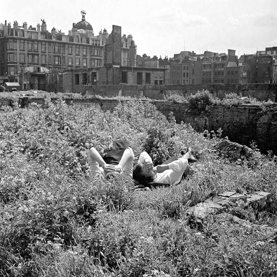 Two women having a rest beside bomb damaged ruins of demolished buildings