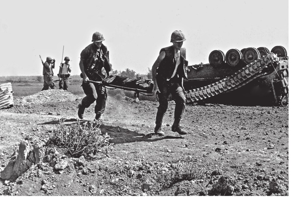  Two 'grunts' running a stretcher with a wounded crewman to the Medivac chopper. A blown-up APC (Armoured Personnel Carrier) sits upside-down in the background