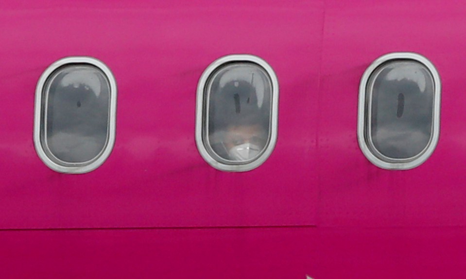  Passengers wearing masks peer out of the windows of a plane as Wizz Air resumed flights from London's Luton Airport on May 1