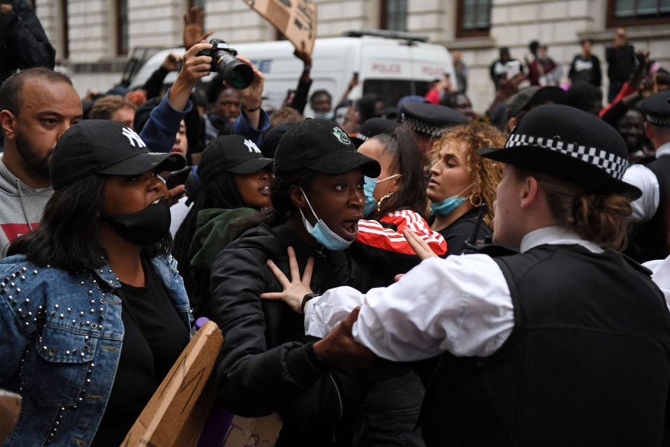  A police officer puts her hands out as protesters in masks draw near