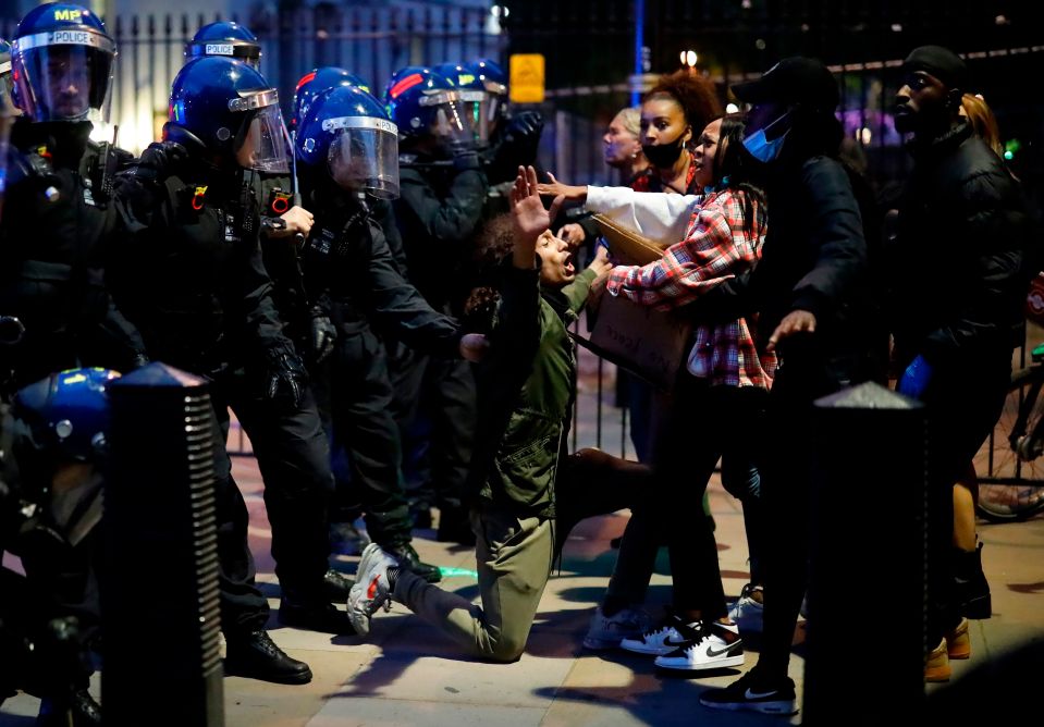  A protester kneels in front of cops in riot gear