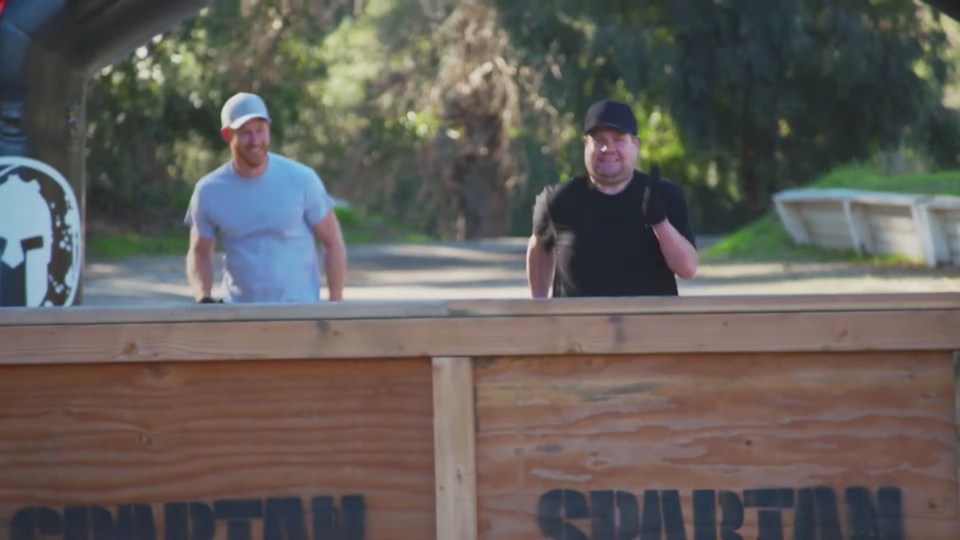 Prince Harry and James Corden running towards a Spartan-branded obstacle.