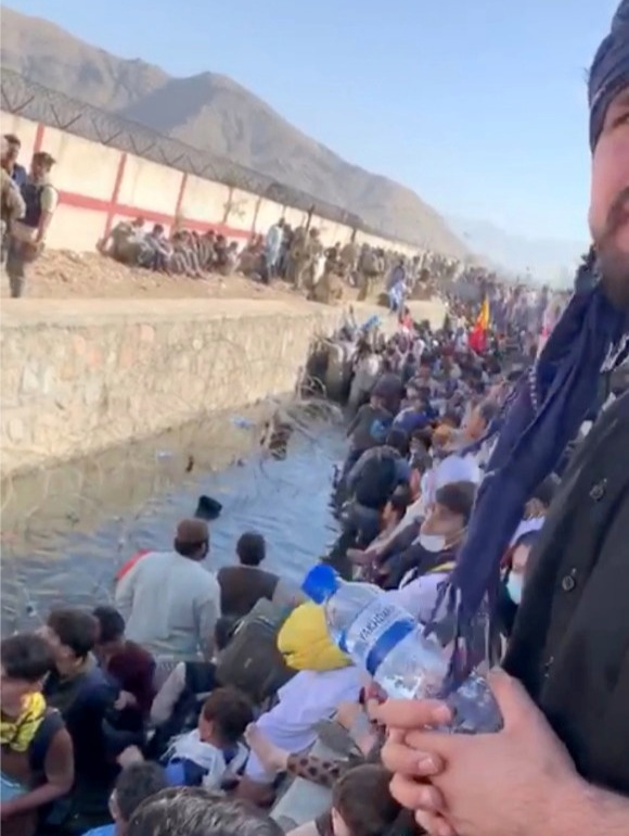 Thousands of people are waiting in a holding pen next to a sewage canal