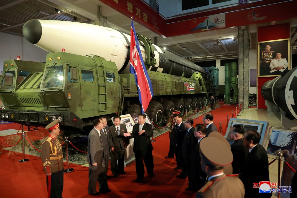 Kim Jong Un speaks to officials next to military weapons and vehicles on display