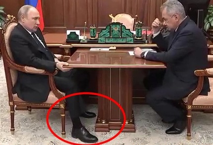 two men are sitting at a table having a conversation . one of the men is wearing a pair of black shoes .