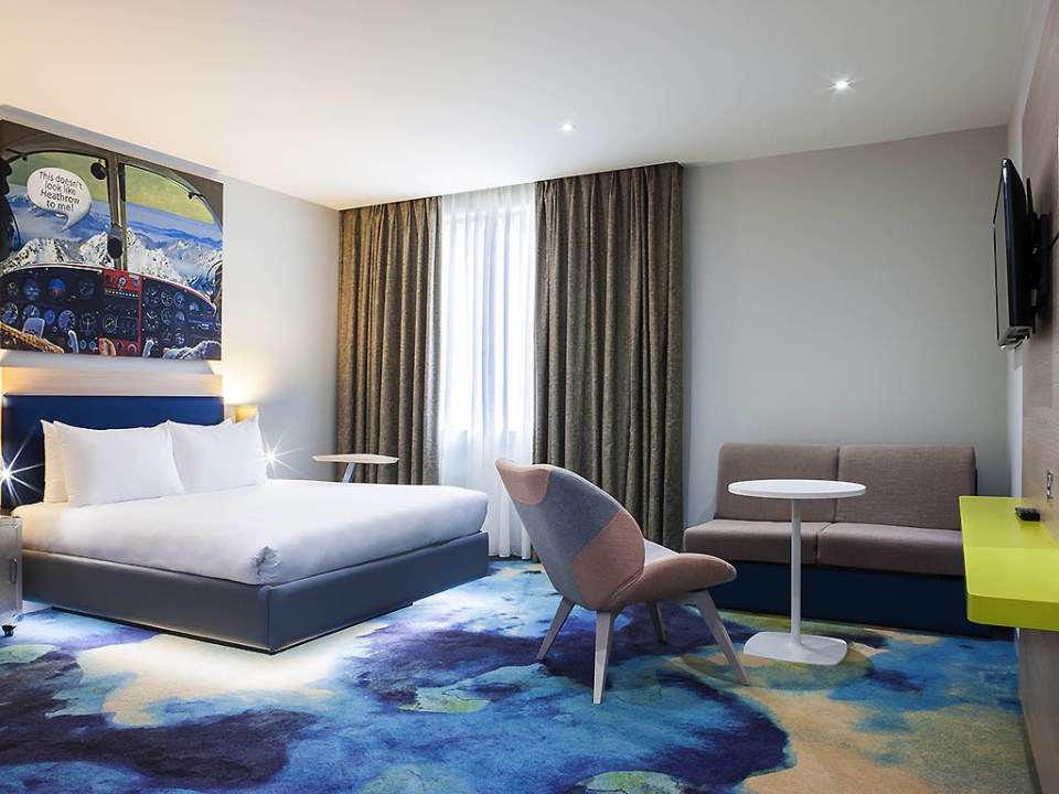 Hotel room with a bed, seating area, and airplane-themed artwork.